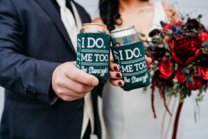 bride and groom holding their beers together with coozy on them