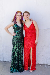2 high school girls wearing prom dresses one is red and one is green 