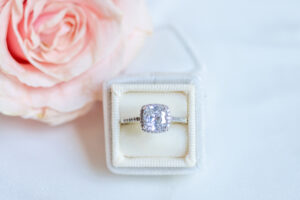 large diamond ring in ring box with a flower nearby